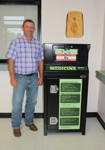 Pictured above, Macon County Sheriff Mark Gammons displays the medication disposal bin located in the lobby of the sheriff’s office. (Photo by: J. Willliams)